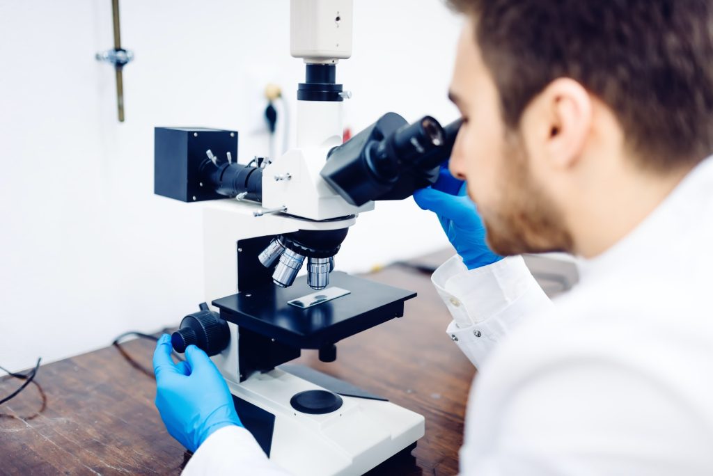 Scientist looking through a microscope in a laboratory, testing samples and probes